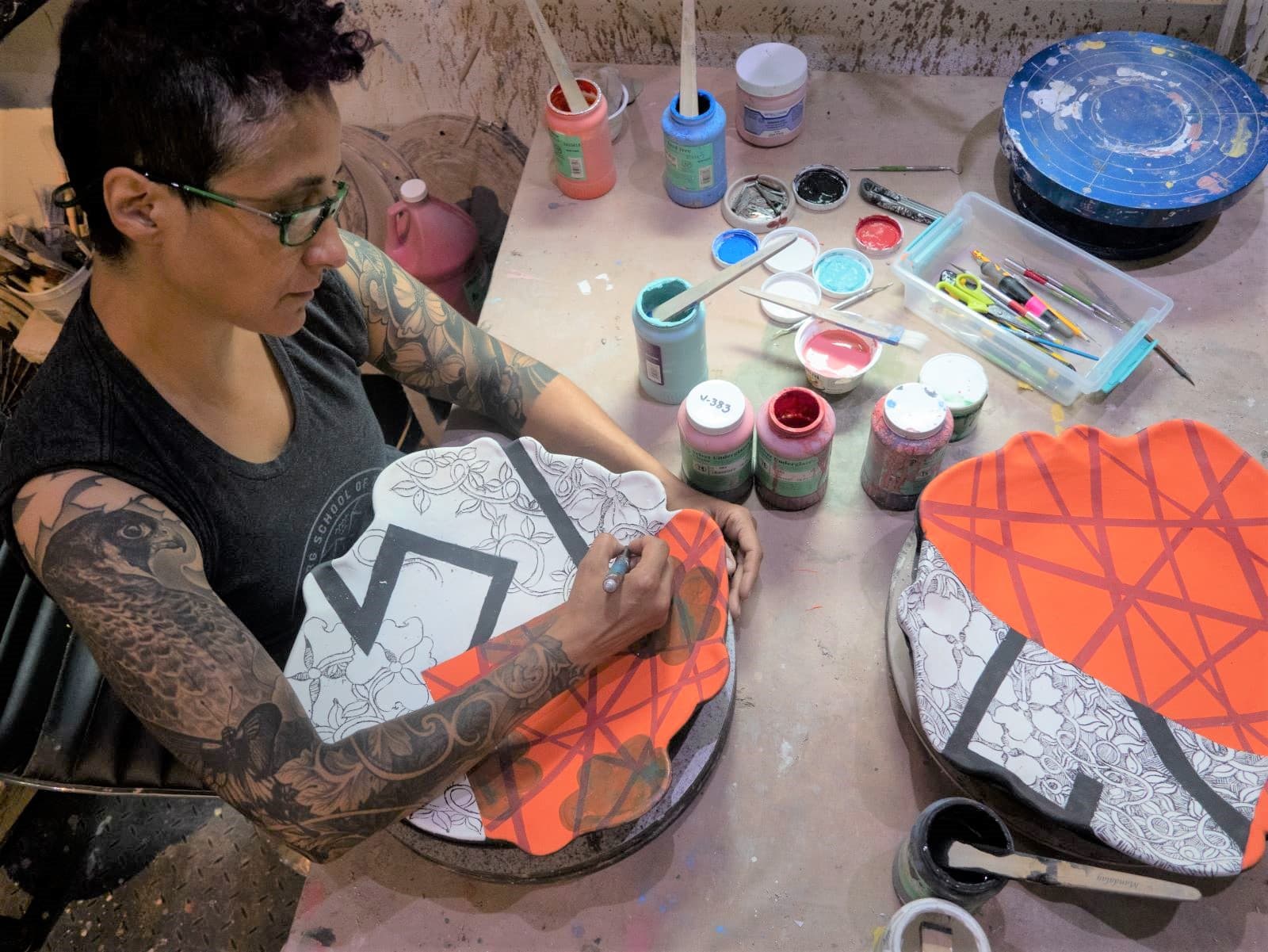 A photo of Adero Willard, a Black American artist, in her studio glazing a ceramic plate.